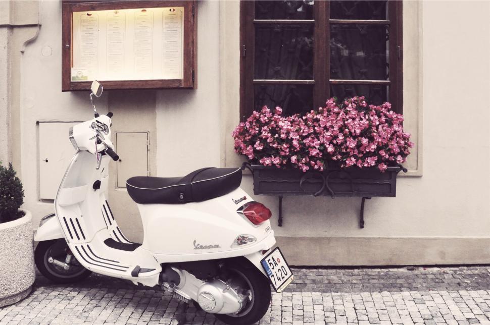 Free Image of Vespa scooter parked by a charming floral facade. 