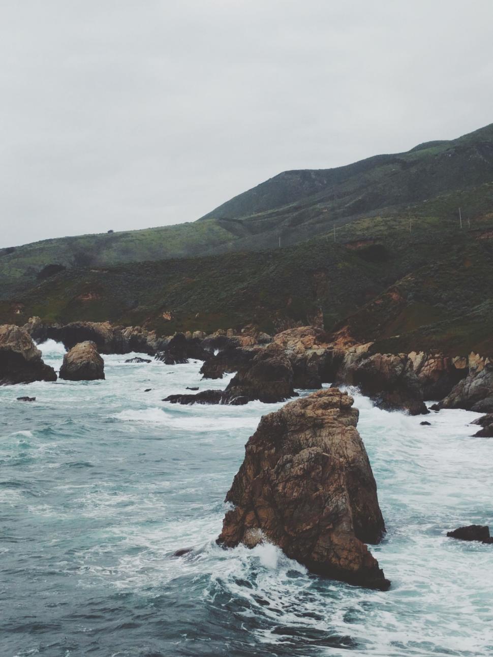 Free Image of Rocky coastline with crashing waves under cloudy sky 