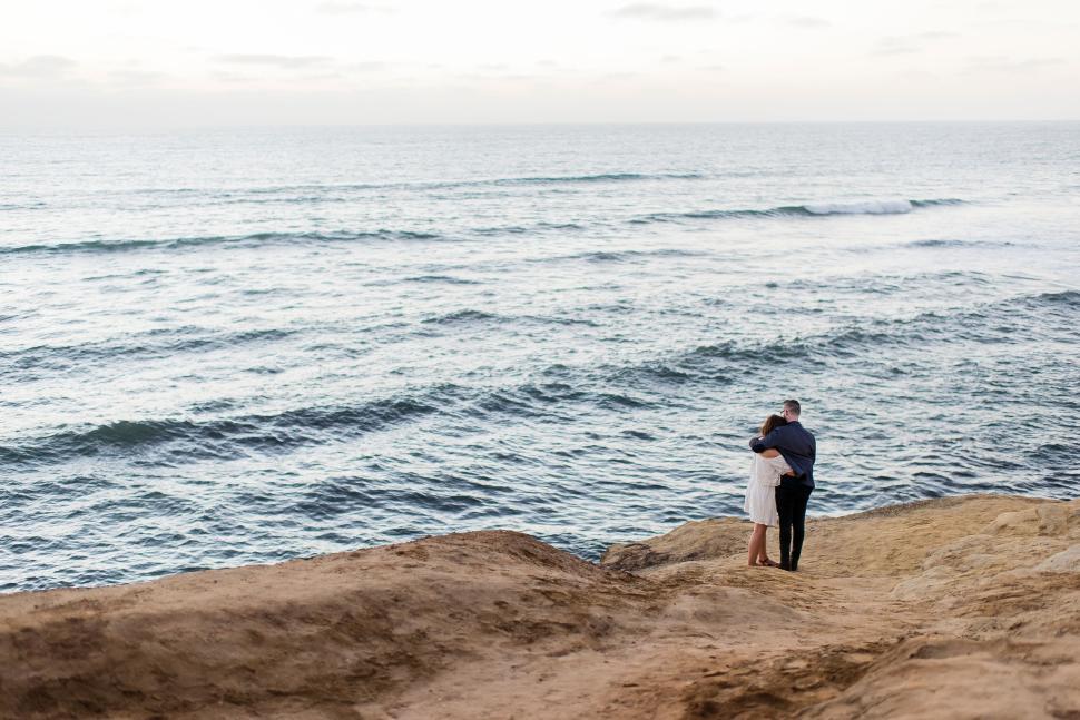 Free Image of Couple embracing on cliffside overlooking the ocean at dusk 