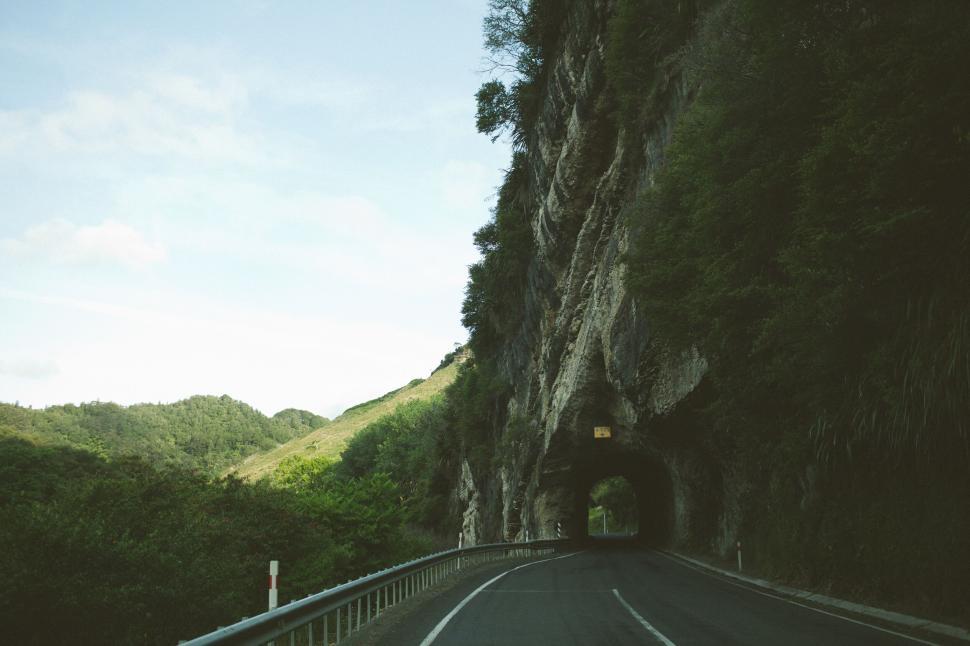 Free Image of Mountain tunnel with curved road under sunny sky 