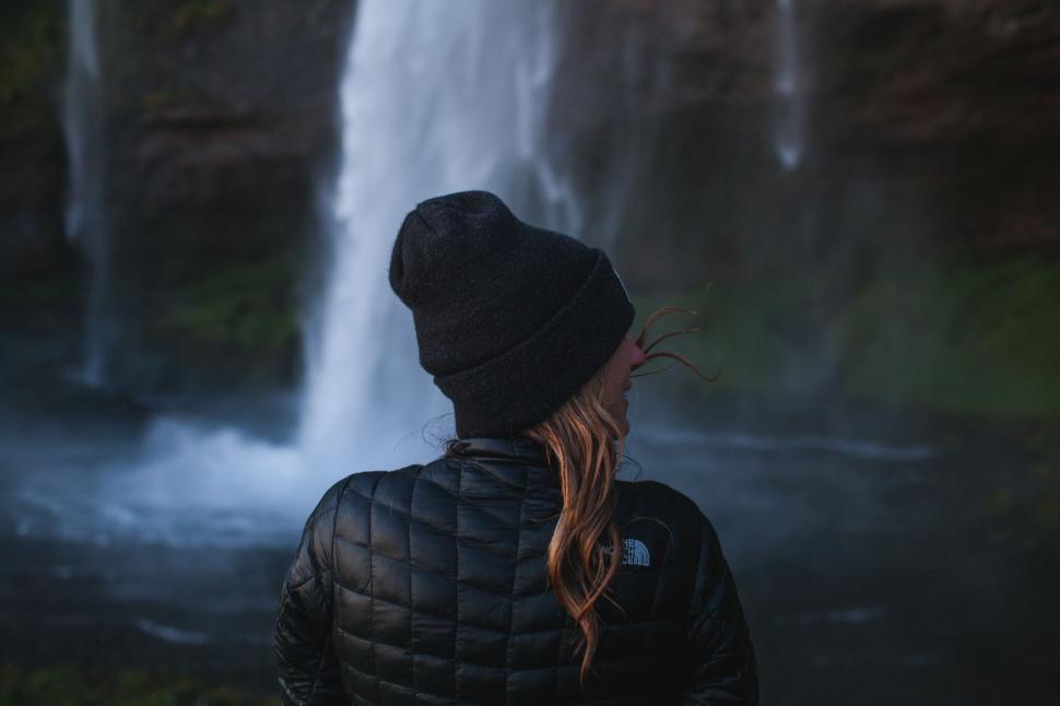 Free Image of Person in jacket and beanie facing a cascading waterfall 