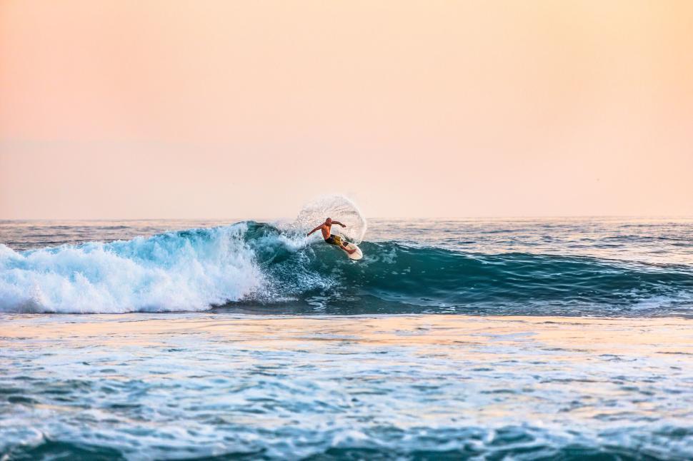Free Image of Surfer riding ocean wave at golden hour with water spray. 