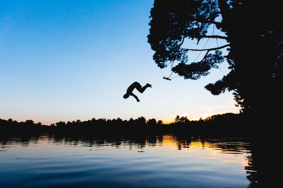 Free Image of Silhouette diving into a lake at sunset over treetops. 