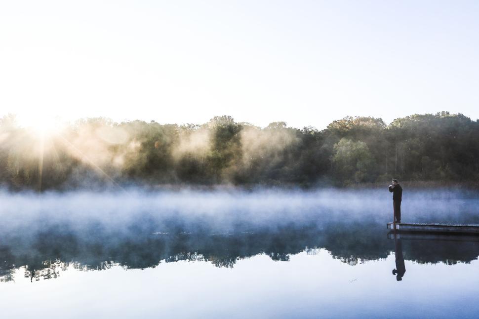 Free Image of Man on dock by misty forest lake at dawn sunlight. 