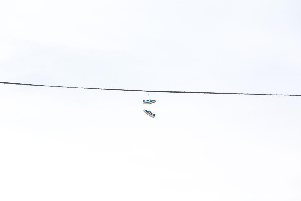 Free Image of Suspended shoes hanging from power line against sky. 