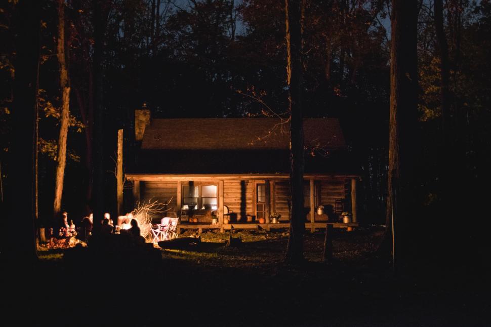 Free Image of Cozy log cabin illuminated by campfire during night. 