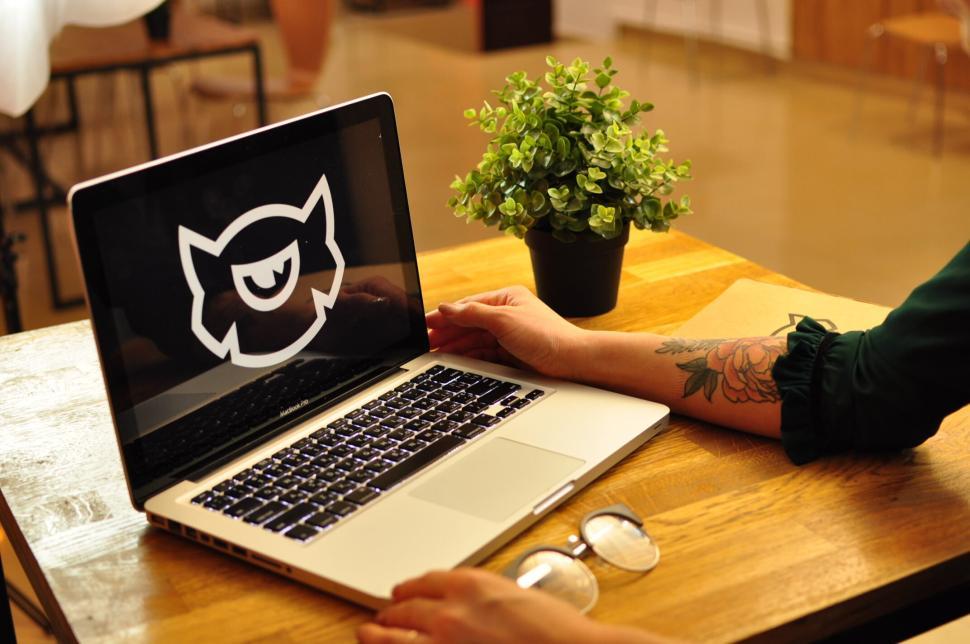 Free Image of Person using laptop with cartoon logo on wooden desk. 