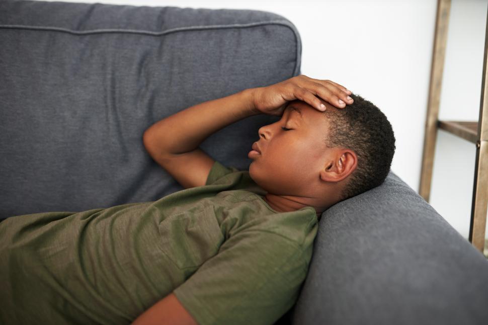 Free Image of Side view closeup portrait of african american boy kid in green t-shirt lying on couch with closed eyes, putting hand on forehead, having fever and flu or suffering from terrible headache 