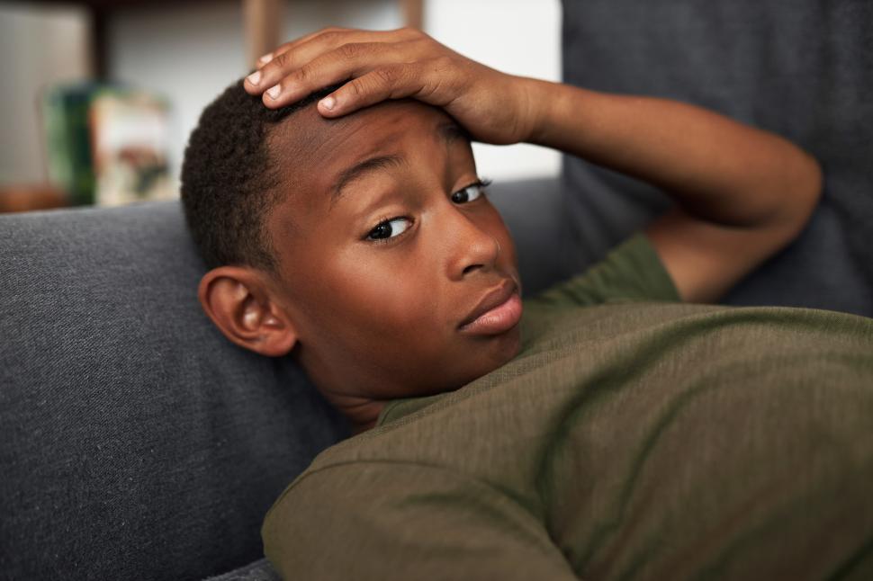 Free Image of Indoor closeup image of bored lazy black kid boy lying on sofa with puzzled facial expression, thinking how spend leisure time without gadgets and internet, looking at camera touching head with hand 