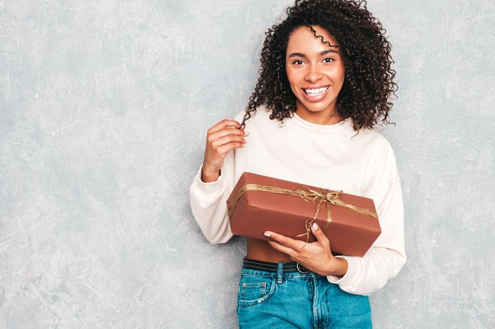 Free Image of Young woman holding gift box, casual indoor setting 