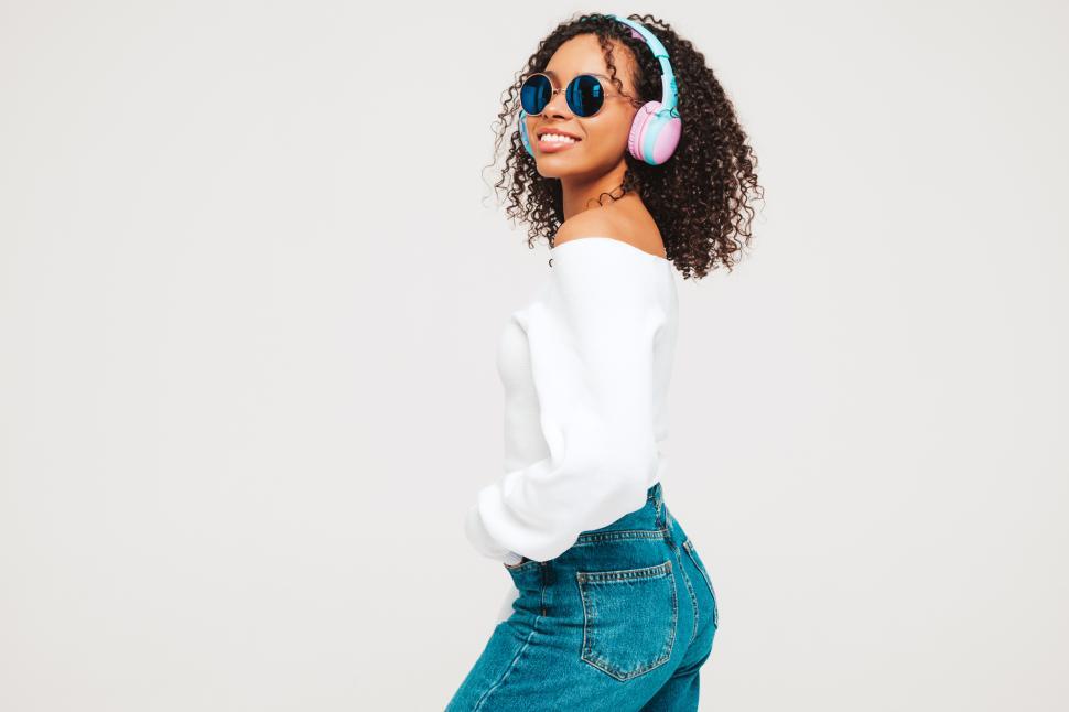 Free Image of Woman in white top and jeans posing with headphones. 