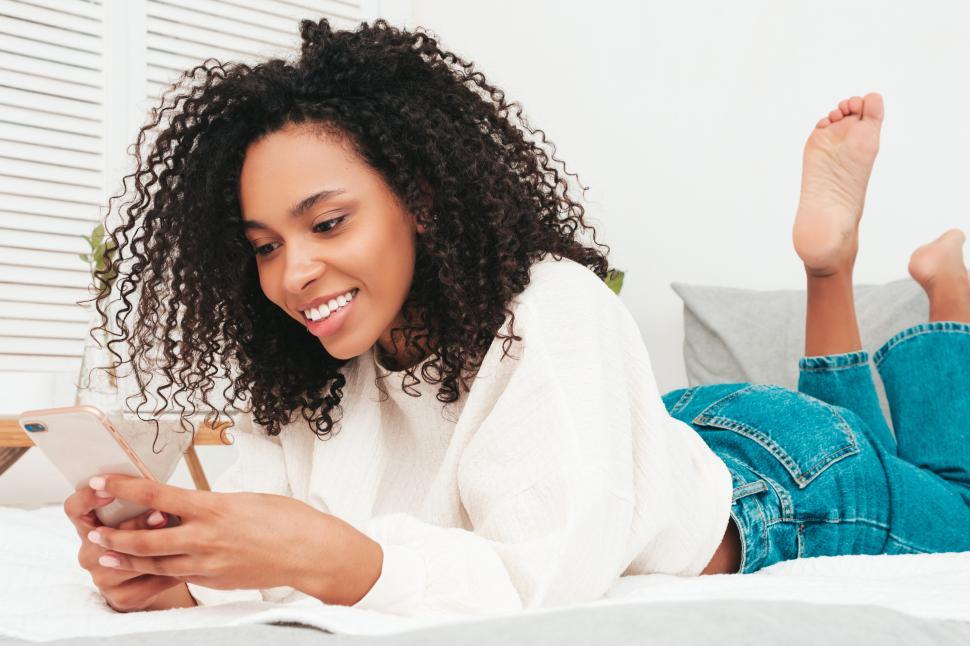 Free Image of Woman lying on bed cheerfully using smartphone. 
