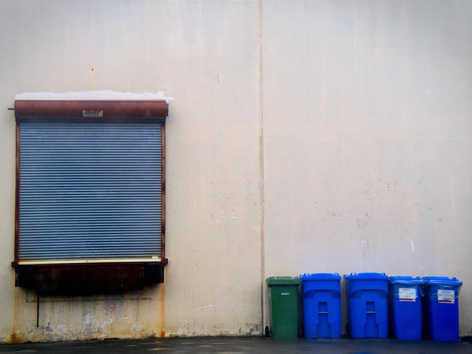 Free Image of Industrial warehouse wall with recycling bins outside. 