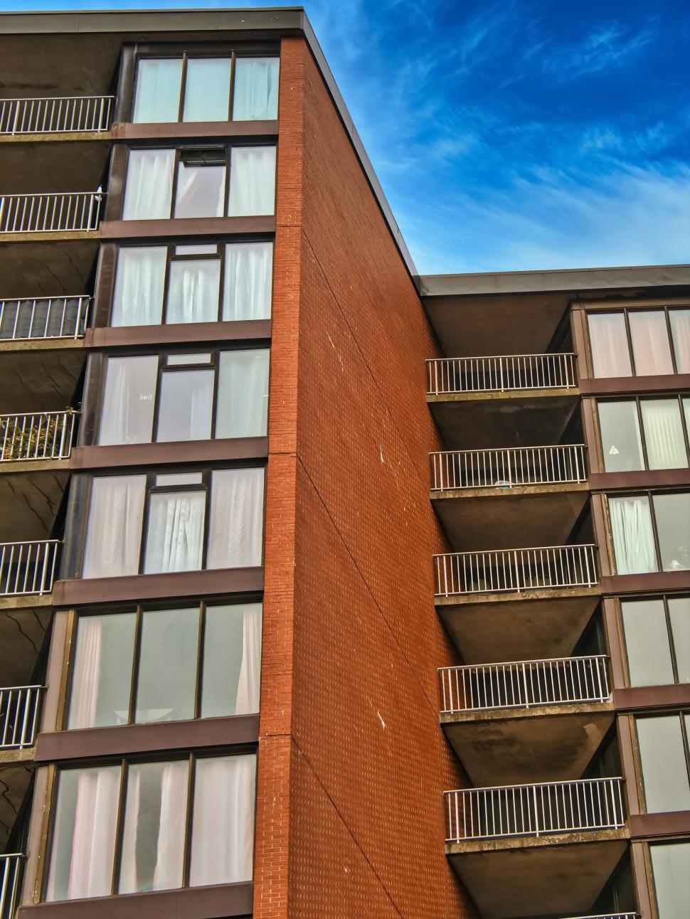 Free Image of Red brick apartment building with glass balconies on facade 