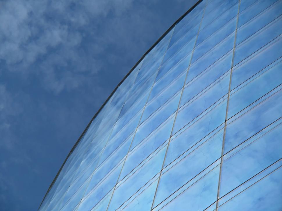 Free Image of Curved glass building reflecting blue sky and clouds 