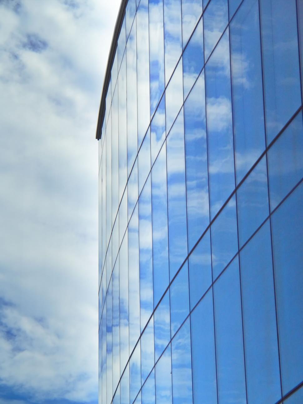 Free Image of Curved glass skyscraper reflecting blue sky and clouds 