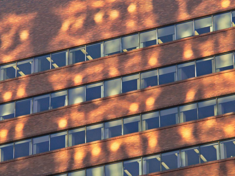 Free Image of Brick building facade with sunlight patterns on windows 