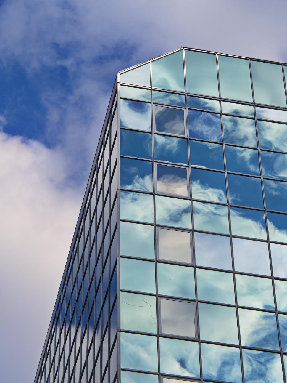 Free Image of Glass building façade reflecting cloudy sky and structures 