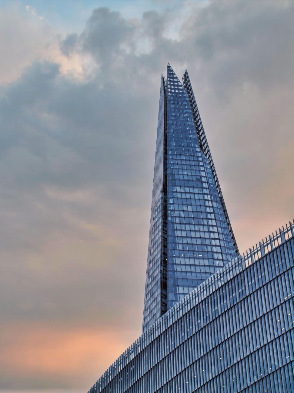 Free Image of Tall glass building with a spire under a dramatic sky 