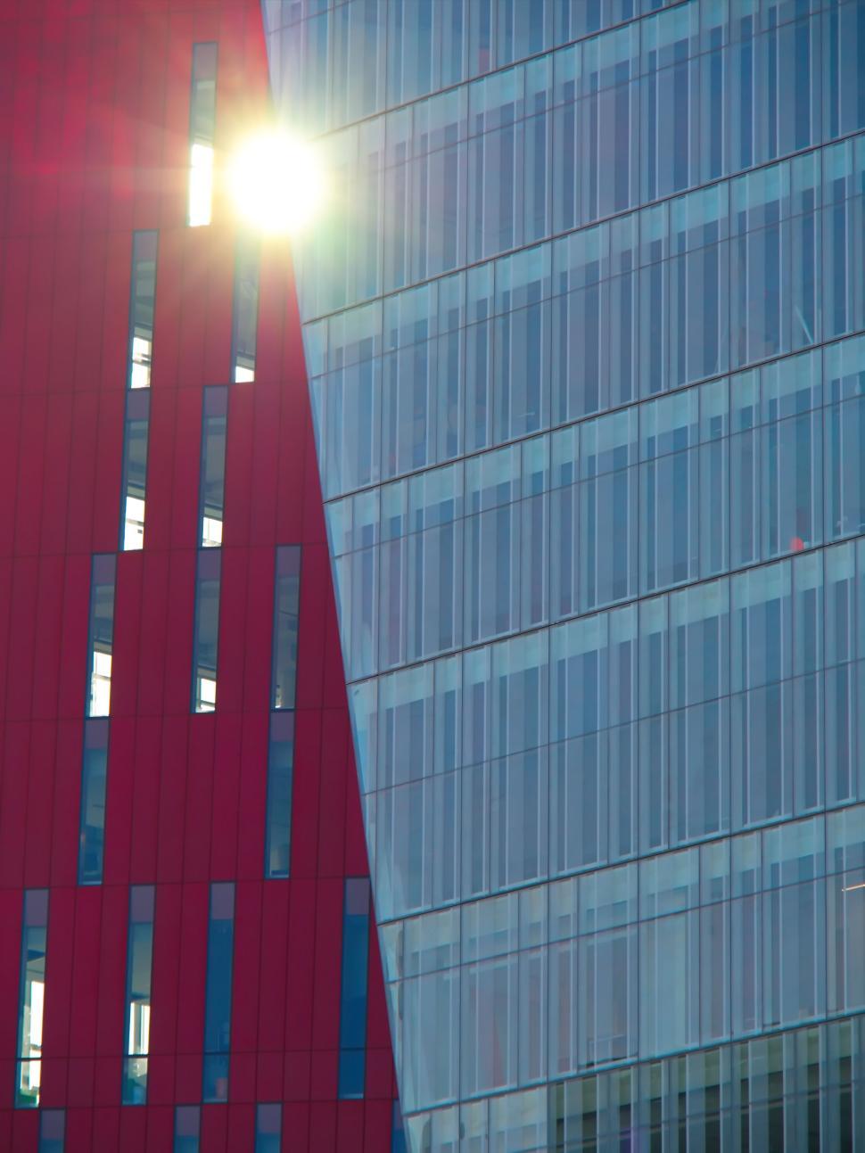 Free Image of Sun shining between red and glass modern buildings 