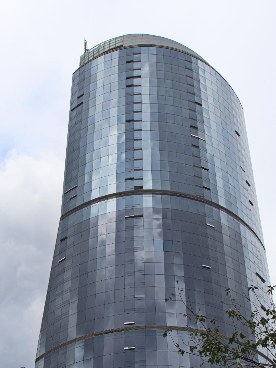 Free Image of Modern cylindrical glass skyscraper against cloudy sky. 