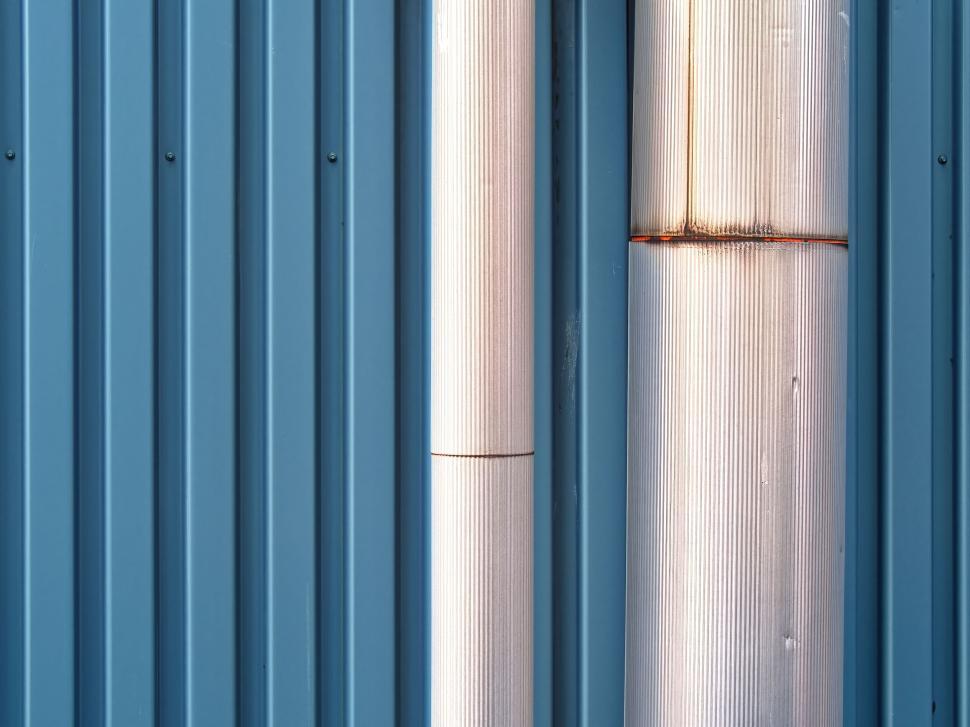 Free Image of Metallic pipes against vertical blue metal panels background. 