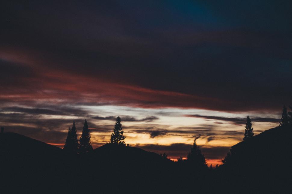 Free Image of Colorful sunset over silhouette of trees and hills 