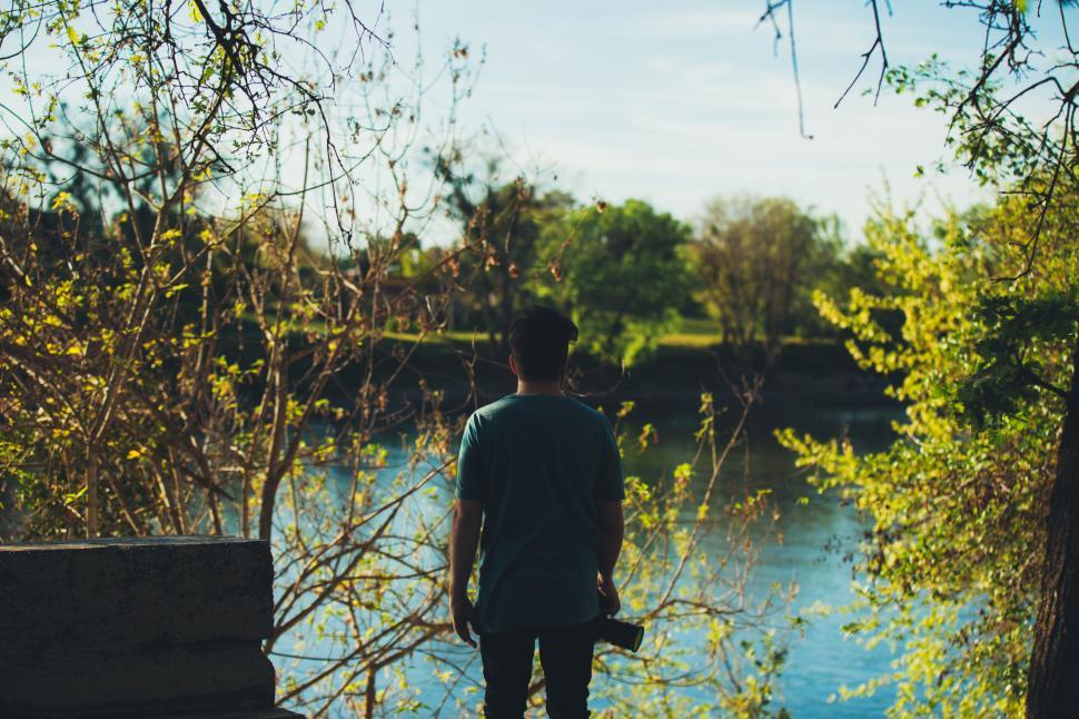 Free Image of Person standing by a serene river surrounded by nature. 