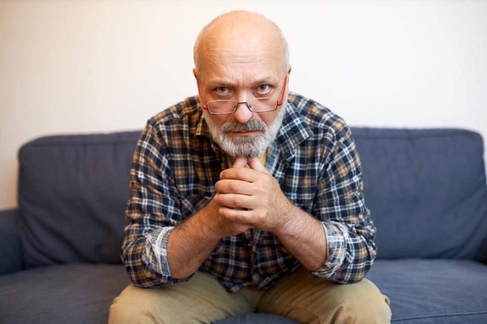 Free Image of Confident decisive furious motivated handsome senior man in glasses sitting on couch with clenched fists under chin looking straight at camera ready to fight and get what he needs and wants 