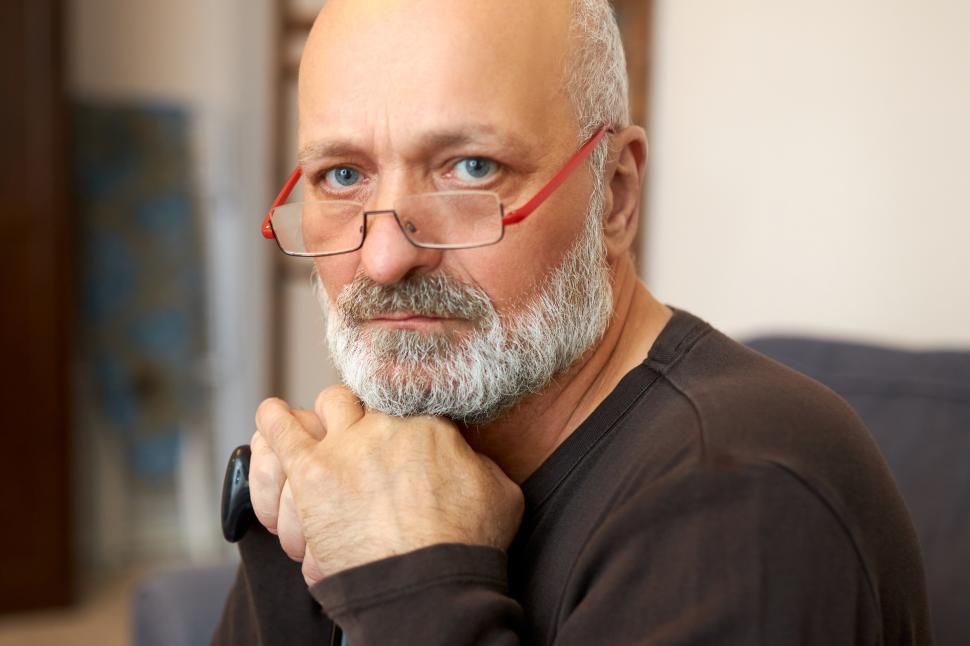 Free Image of Closeup portrait of wealthy rich senior businessman in glasses with gray beard looking at camera with upset sad facial expression, leaning chin on hands and walking stick, suffering arthritis 