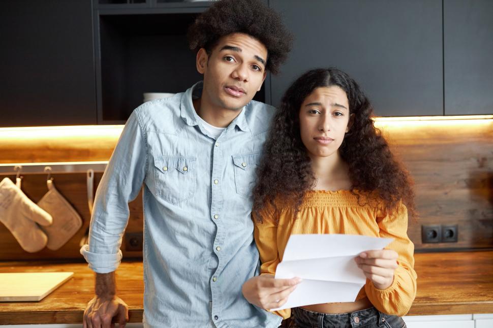 Free Image of Indoor portrait of upset young african american couple upset with high prices on rent standing in kitchen, sad female holding paper document and looking at camera, feeling bankrupt 