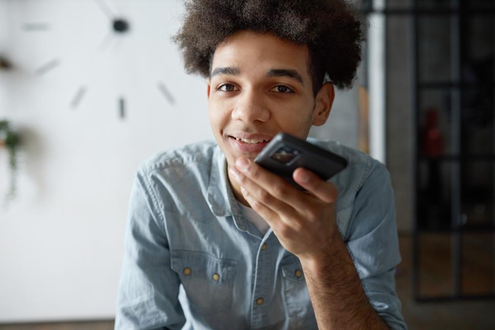 Free Image of Indoor portrait of young african american man recording audio message chatting with friend in messenger on phone. Afro man in shirt dictating commands and recording notes on smartphone voice recorder 