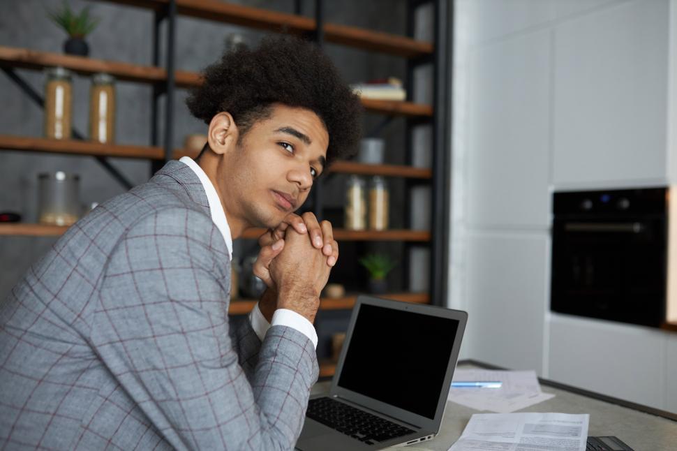 Free Image of Side view of pensive young african american trader sitting at kitchen table in front of laptop with copy space screen looking aside with facial expression full of aspirations and expectations 