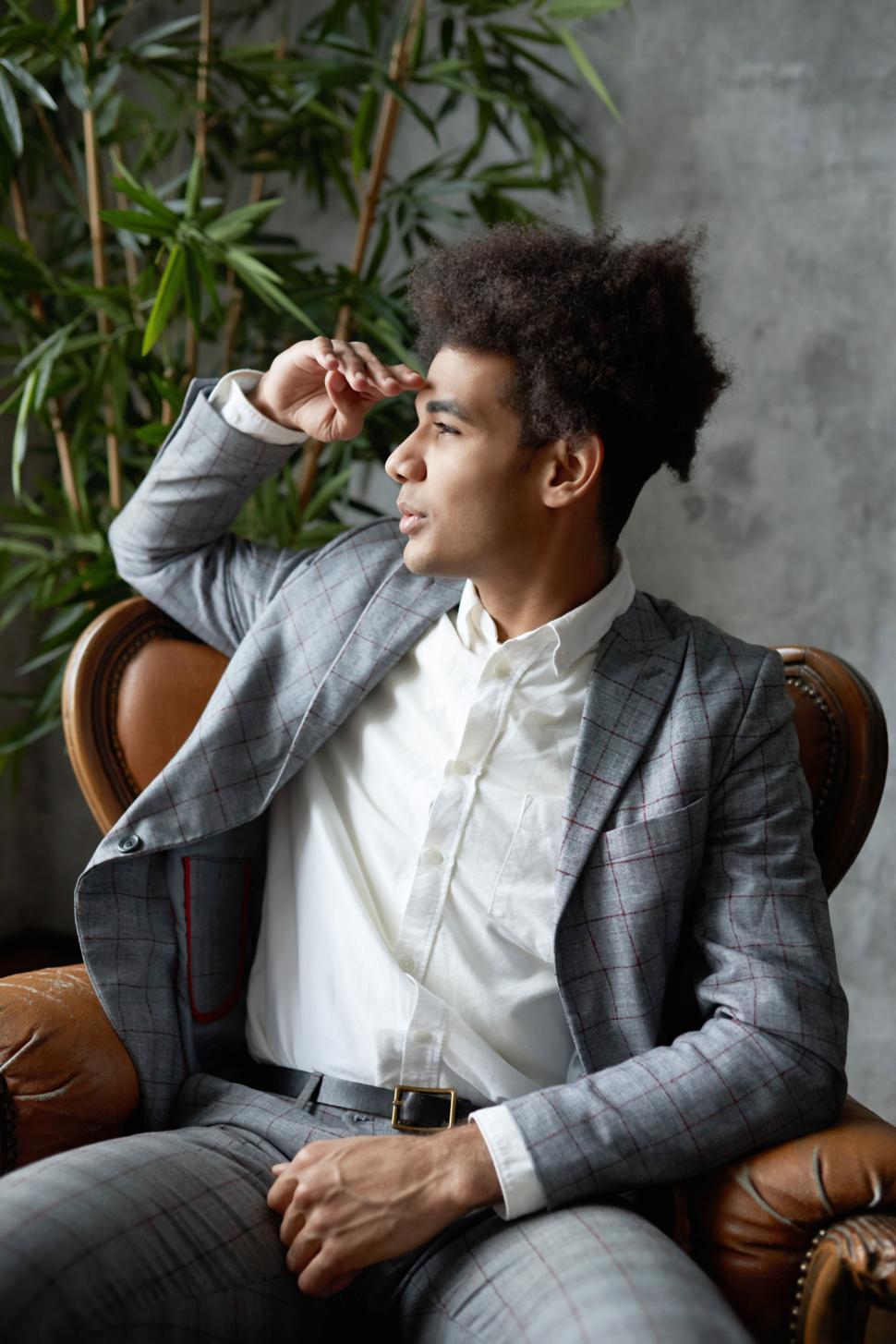 Free Image of Side view of young wealthy successful black businessman with afro hair in elegant suit sitting in armchair holding his hand on forehead and looking forward in future with aspirations and expectations 