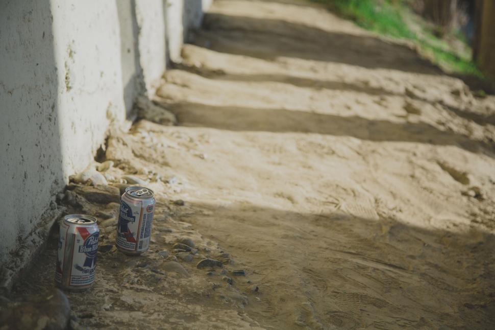 Free Image of Two beer cans left on a sunlit dirt pathway near bridge 