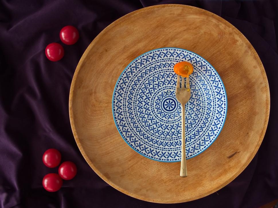 Free Image of Single slice of tomato on a fork against patterned plate. 