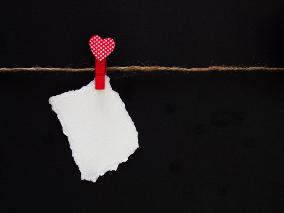 Free Image of Red heart-shaped clip holding a blank white paper note 