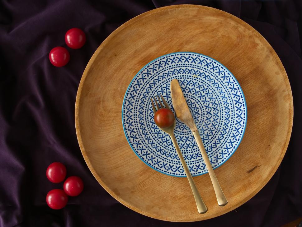 Free Image of Wooden plate with ornate blue-white plate, cutlery, tomatoes 