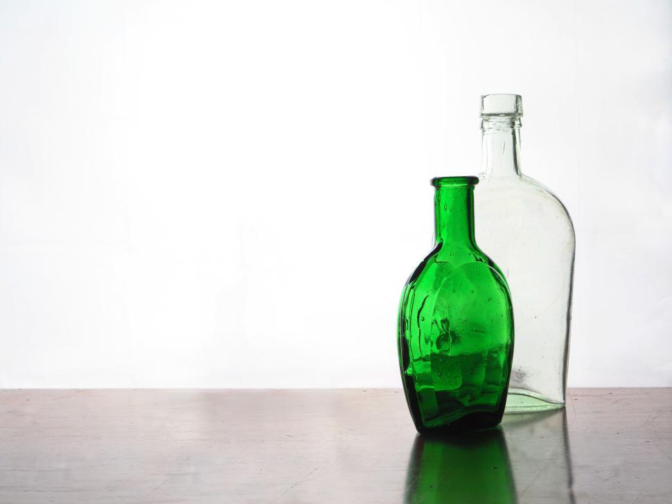 Free Image of Two glass bottles, green and clear, with reflection on surface 