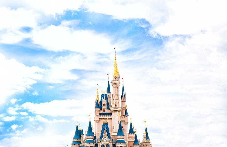 Free Image of Disney castle with blue and golden towers under cloudy sky. 