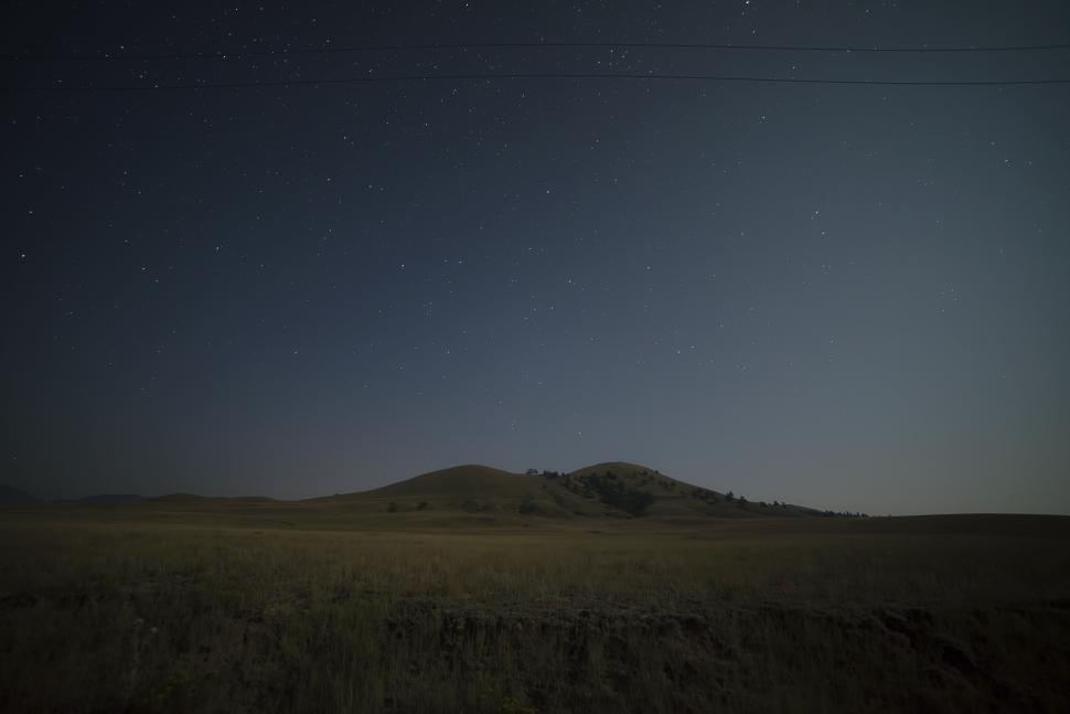 Free Image of Starry night sky above a tranquil hilly landscape. 