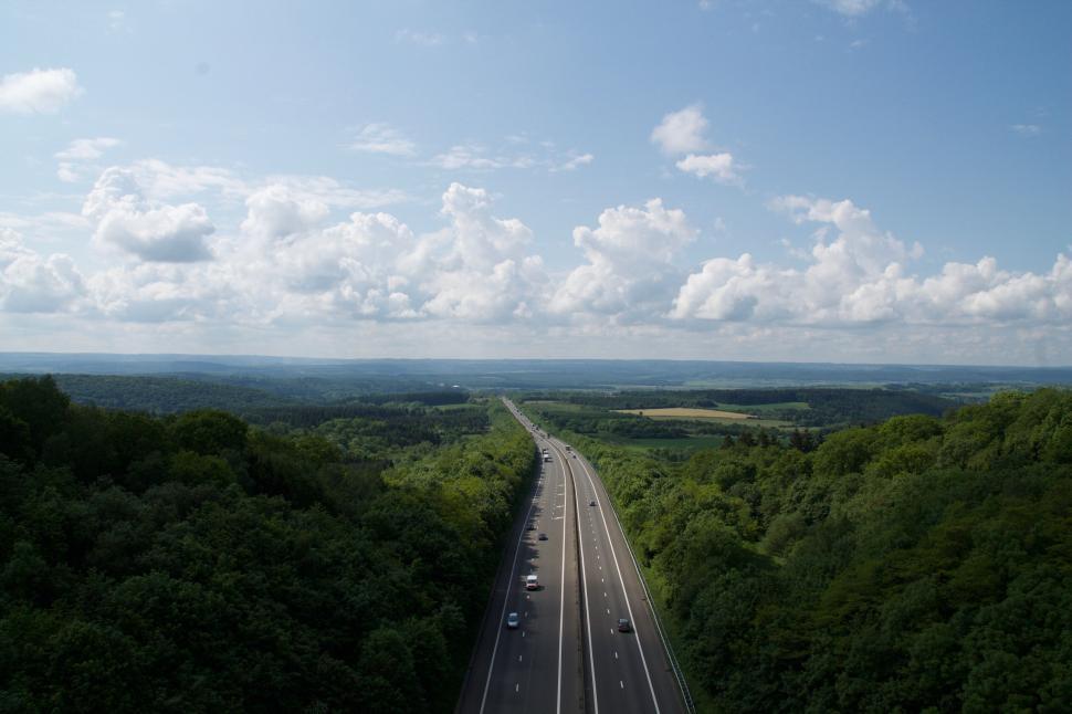 Free Image of Long highway stretching through green forest under sky 