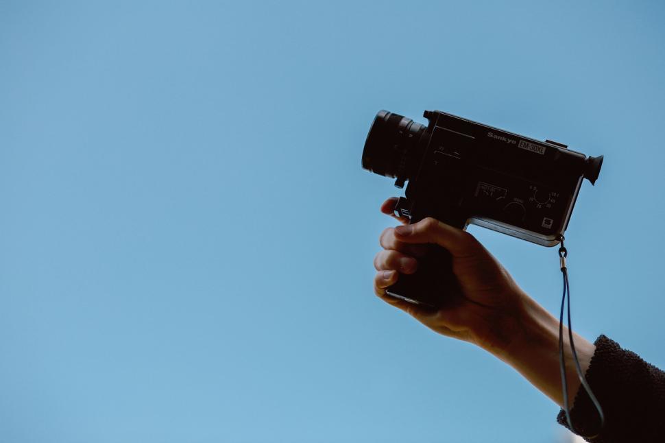 Free Image of Hand holding a retro black camera against clear blue sky 