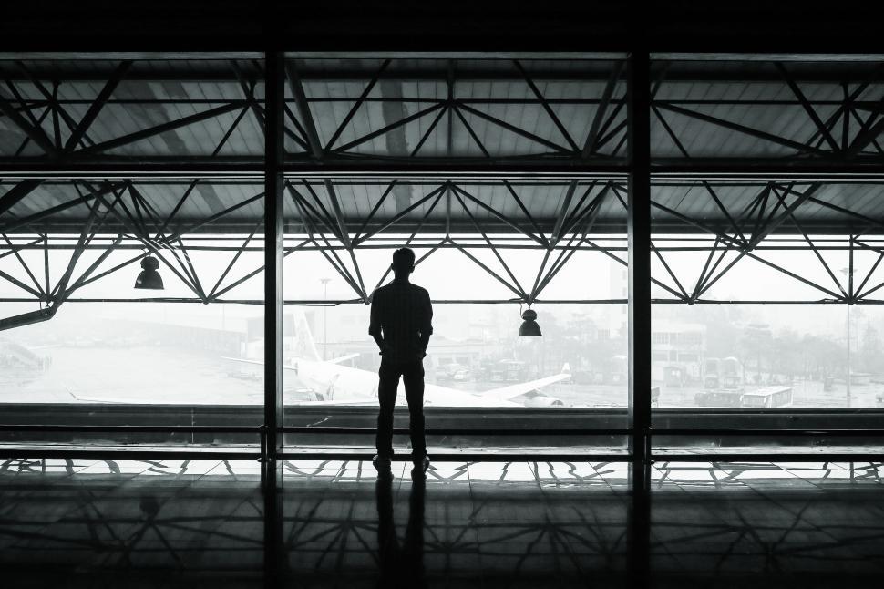 Free Image of Silhouette of a man standing in front of large windows. 