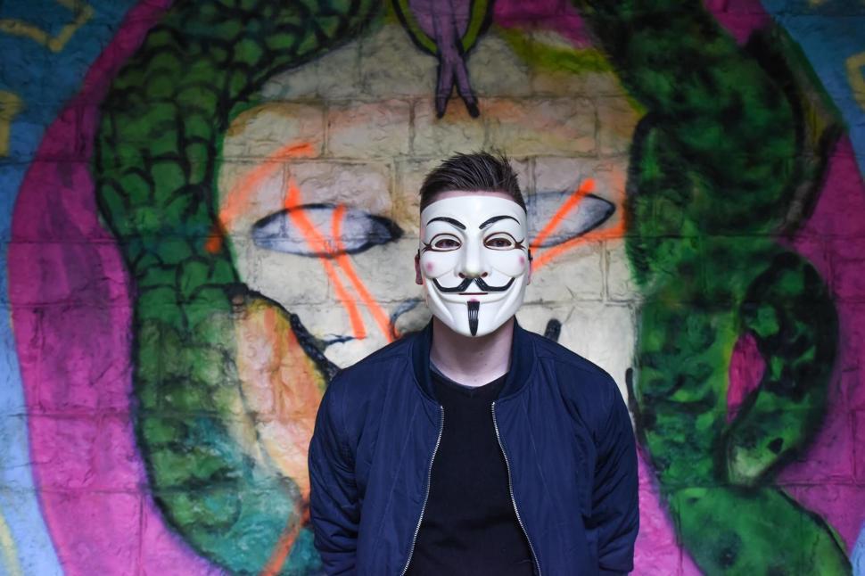 Free Image of Masked individual in front of colorful graffiti artwork. 
