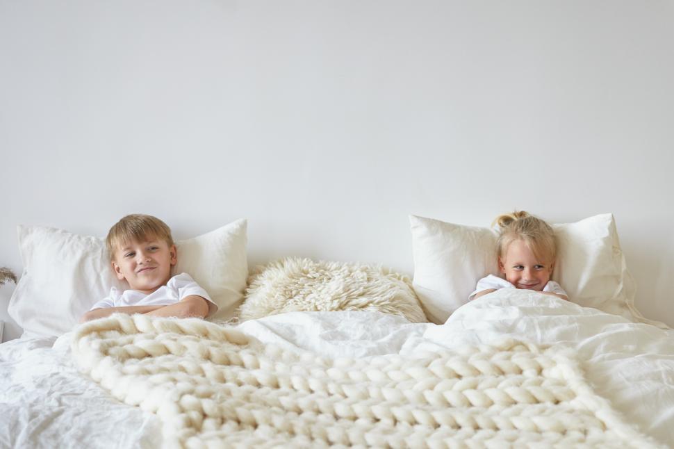 Free Image of Two cute children relaxing in bedroom. Indoor shot of teen boy in pajamas lying on bed with his blonde little brother on the other side, having playful looks. Childhood, kids and family concept 