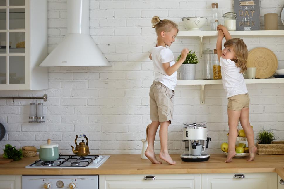 Free Image of Two restless fidgety children wearing casual clothes standing barefooted on kitchen counter, searching for hidden sweets. Cute blonde little boy playing at home with his adorable baby sister 