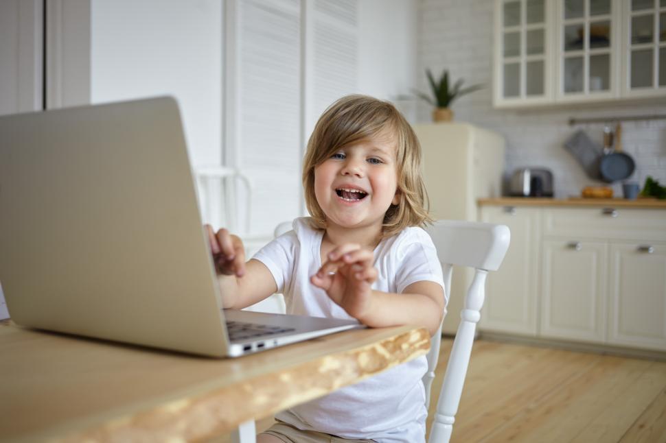 Free Image of Childhood, modern technology, communication and internet addiction concept. Adorable cute baby girl spending too much time in front of laptop, watching video blog, sitting at table and laughing 