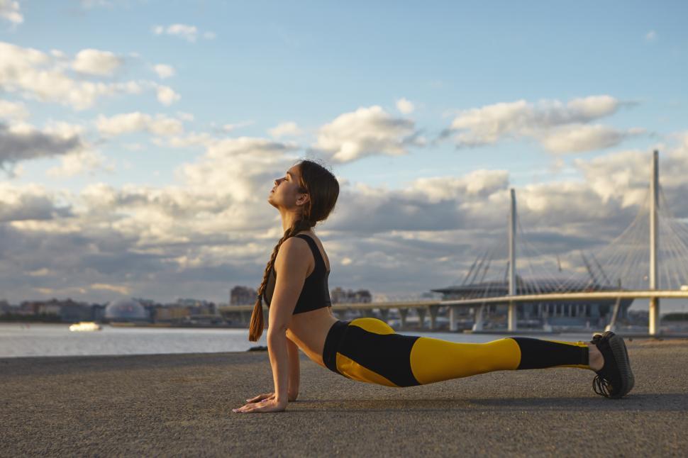 Free Image of Health, activity and wellbeing concept. Beautiful young sportswoman with strong arms exercising against river background, doing yoga, practicing upward facing pose or Urdhva Mukha Svanasana 