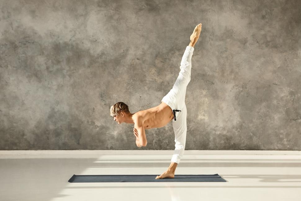 Free Image of Athletic fit young male with muscular torso wearing no shirt practicing advanced yoga asana, standing with one leg on floor, training balance, concentration and coordination, bending forward 